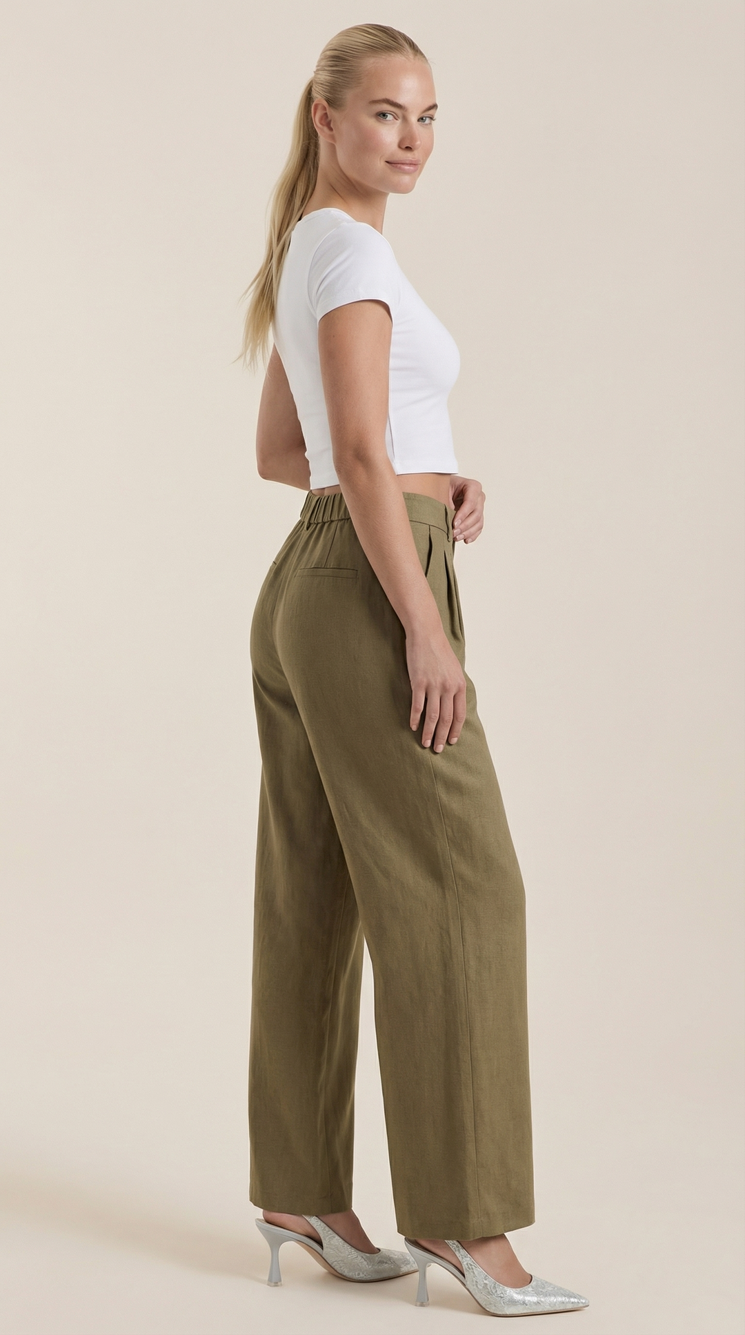 Woman in flowy high-rise pants side view plain background.