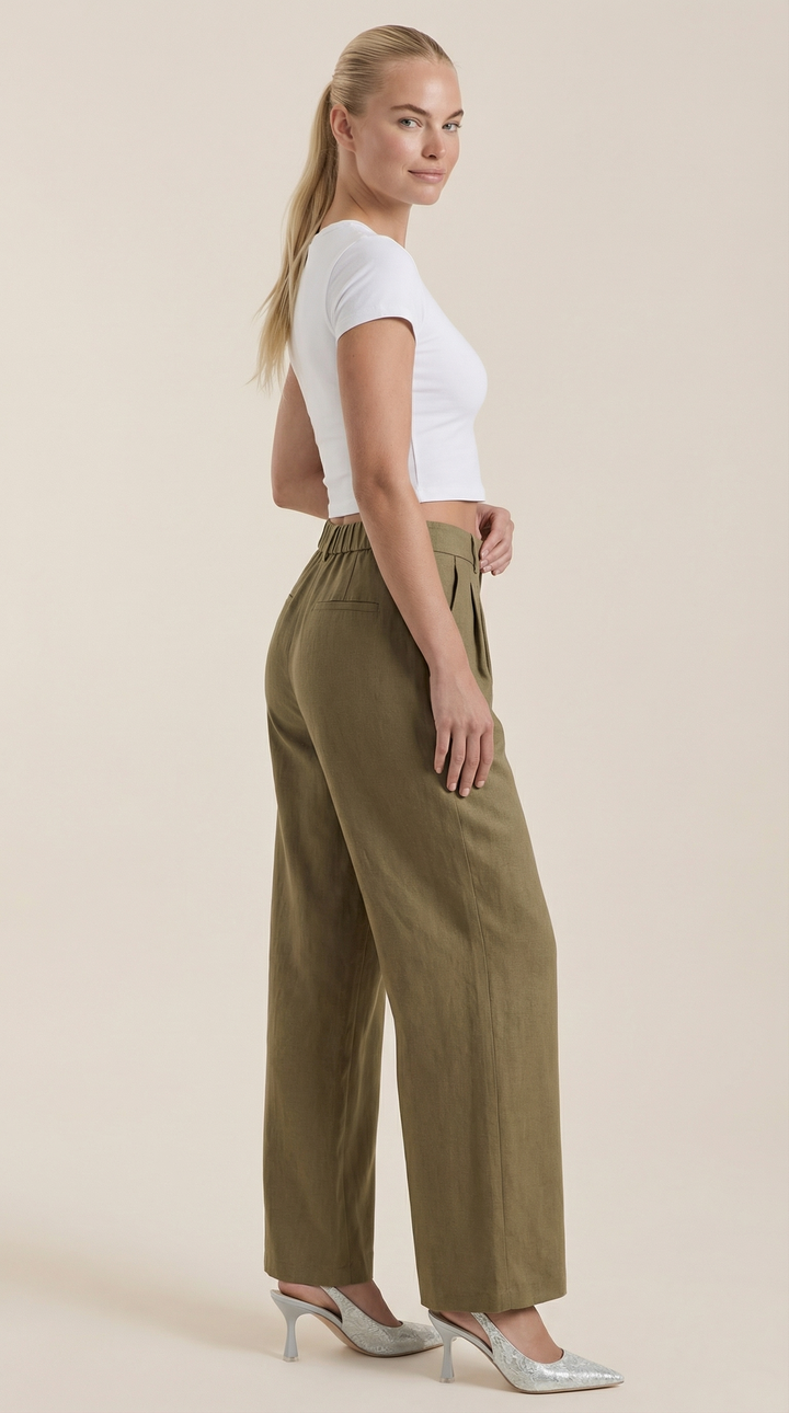 Woman in flowy high-rise pants side view plain background.