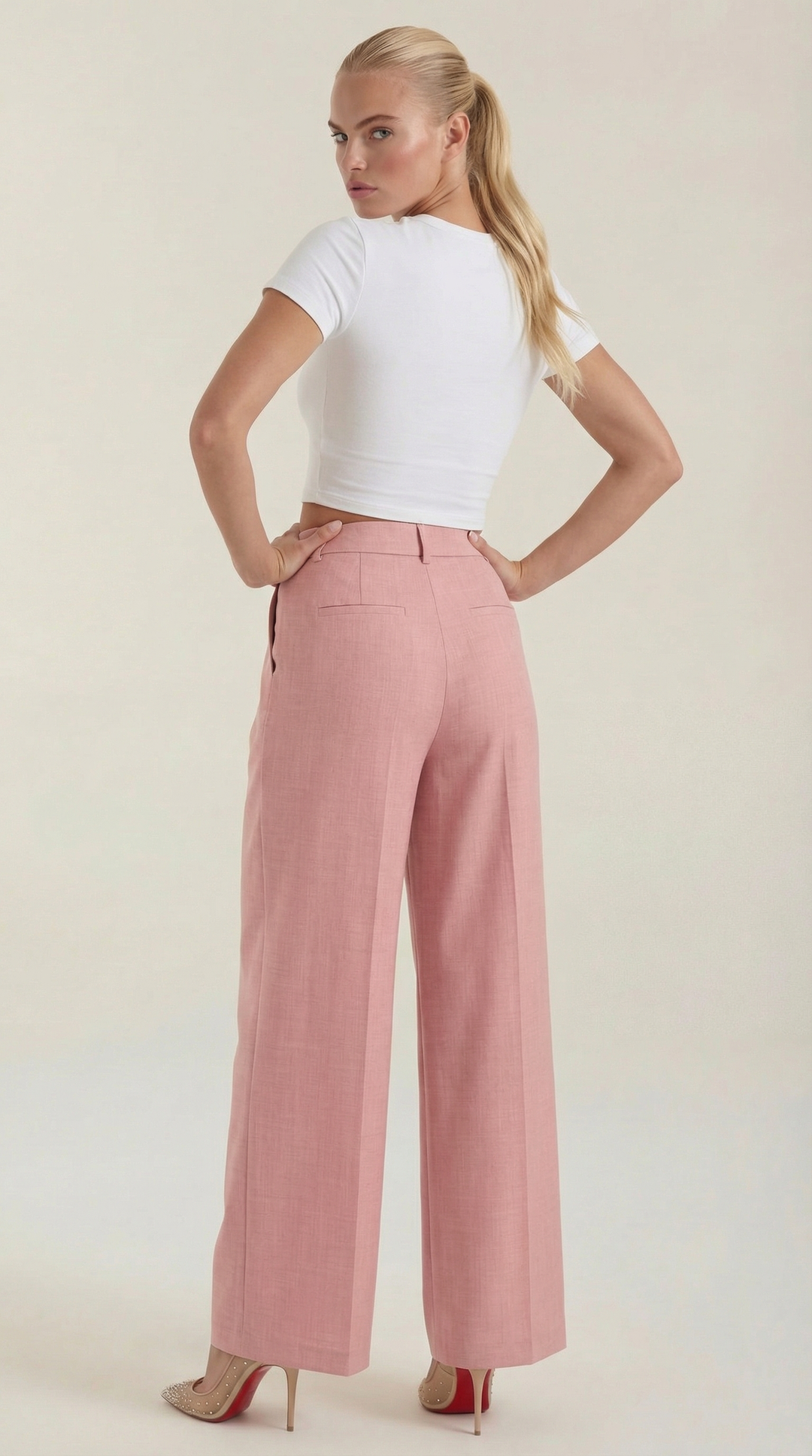Woman posing with pleated front pants on plain background, back view