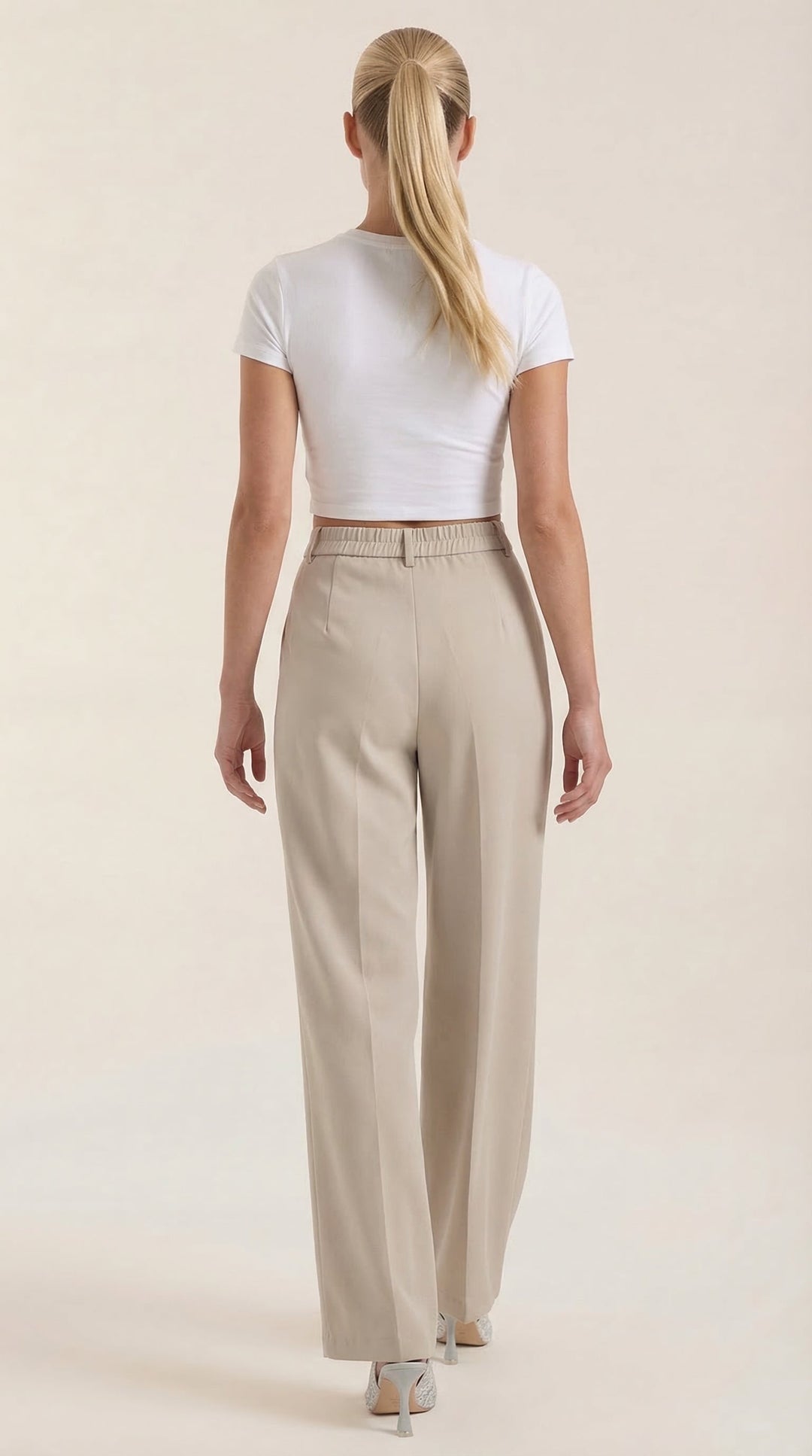 Female model wearing high-rise pants, back view, plain background.