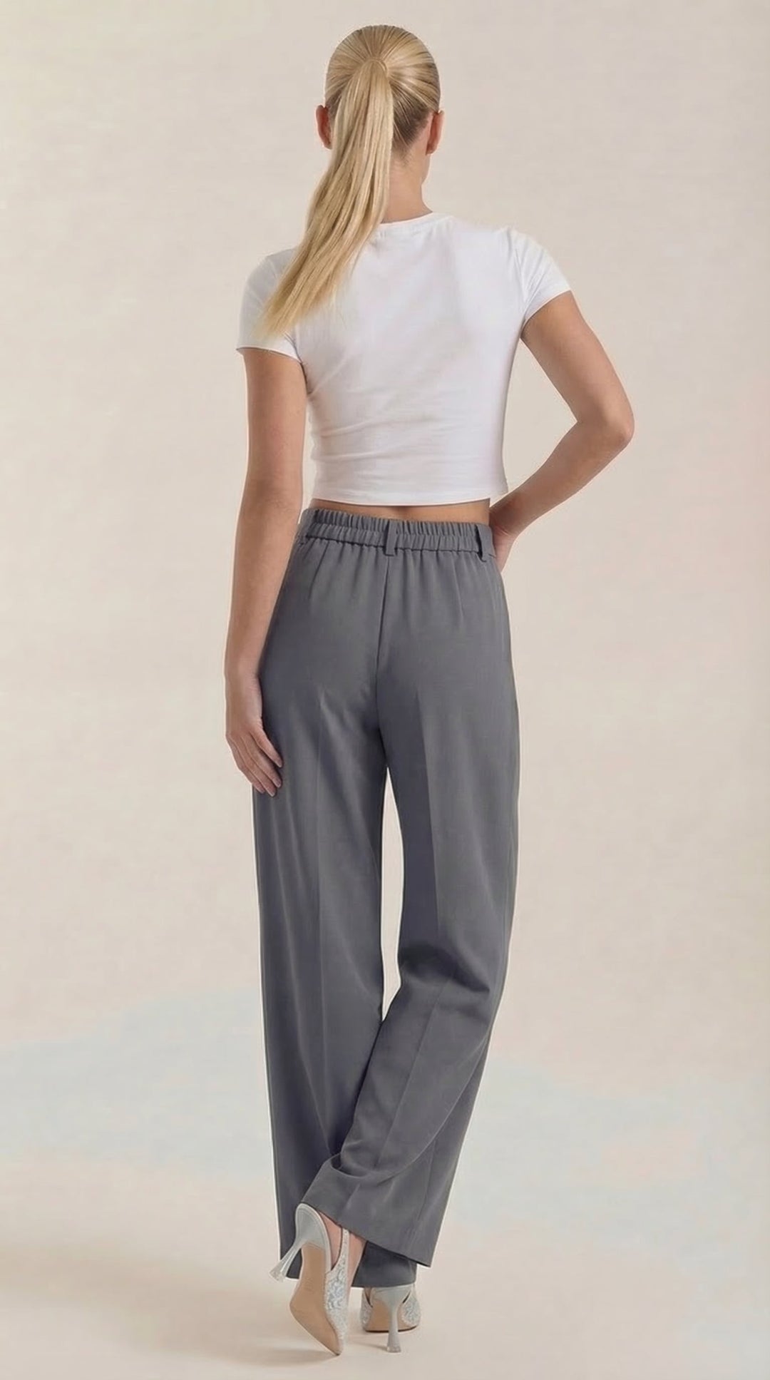 Female model standing sideways in flowing trousers, plain background -backview