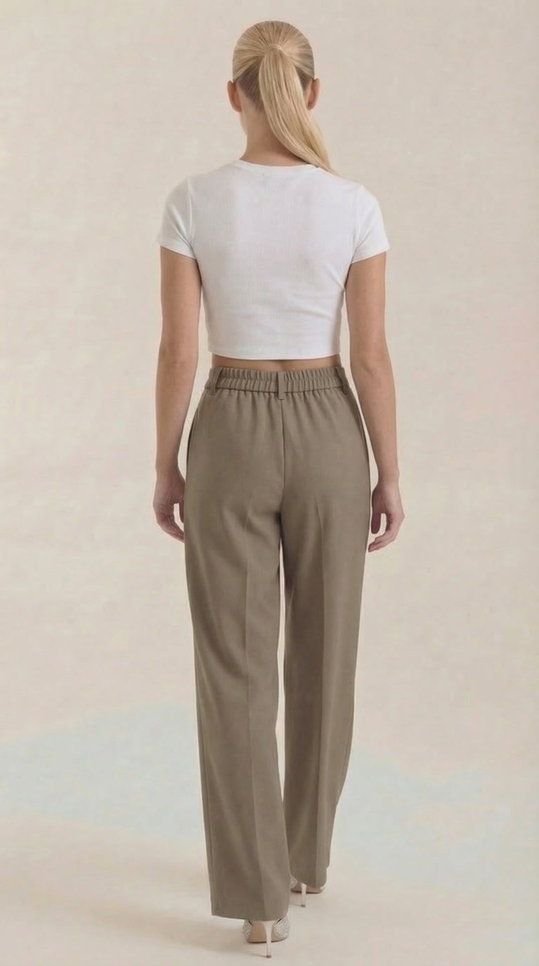 Female model showing straight posture in wide trousers, plain background, back view