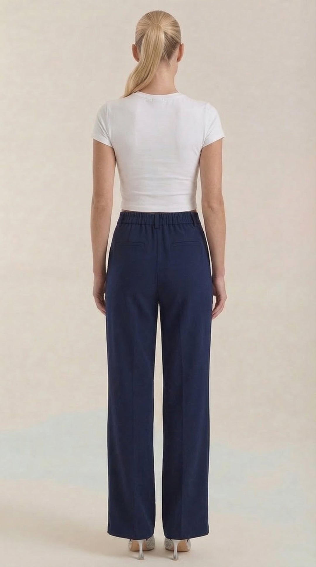 Female model standing in formal trousers on a plain background, back view