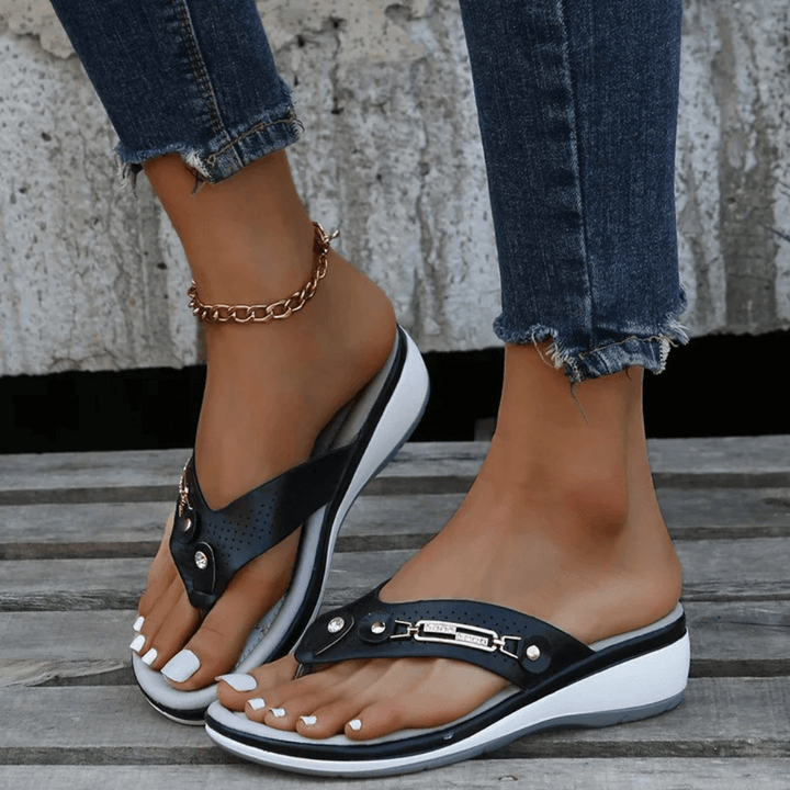 Foot model wearing elegant summer flip-flops on nature background.