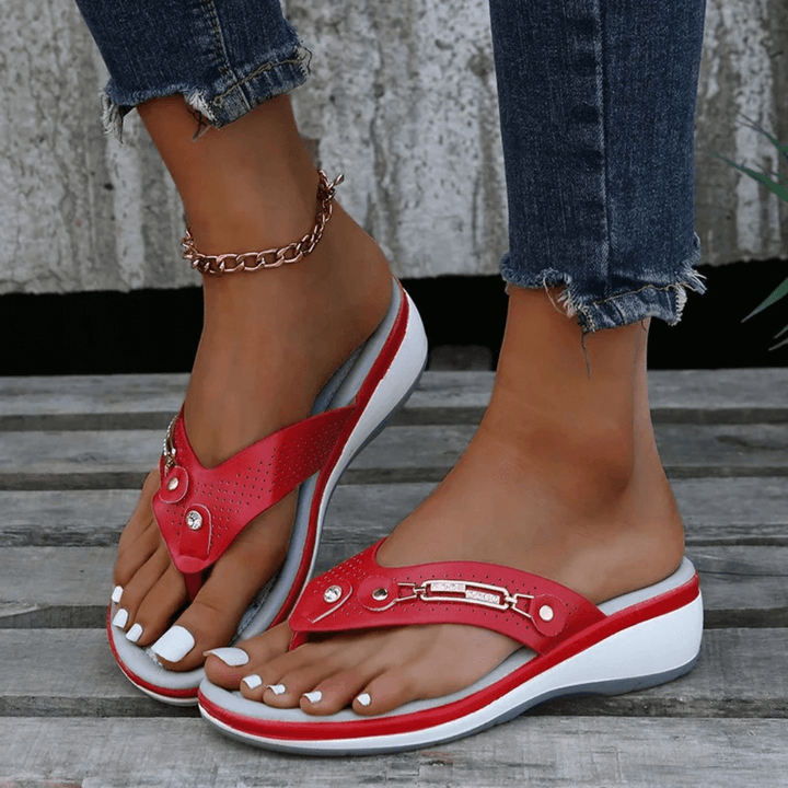 Foot model posing in chic flip-flops against plain natural background.