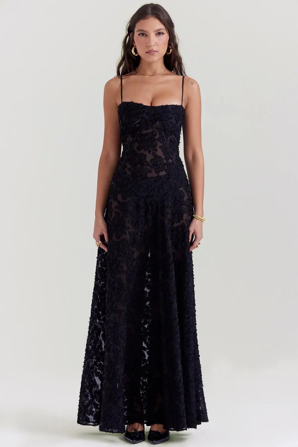 Woman wearing a flowing maxi dress with open back against a plain background.