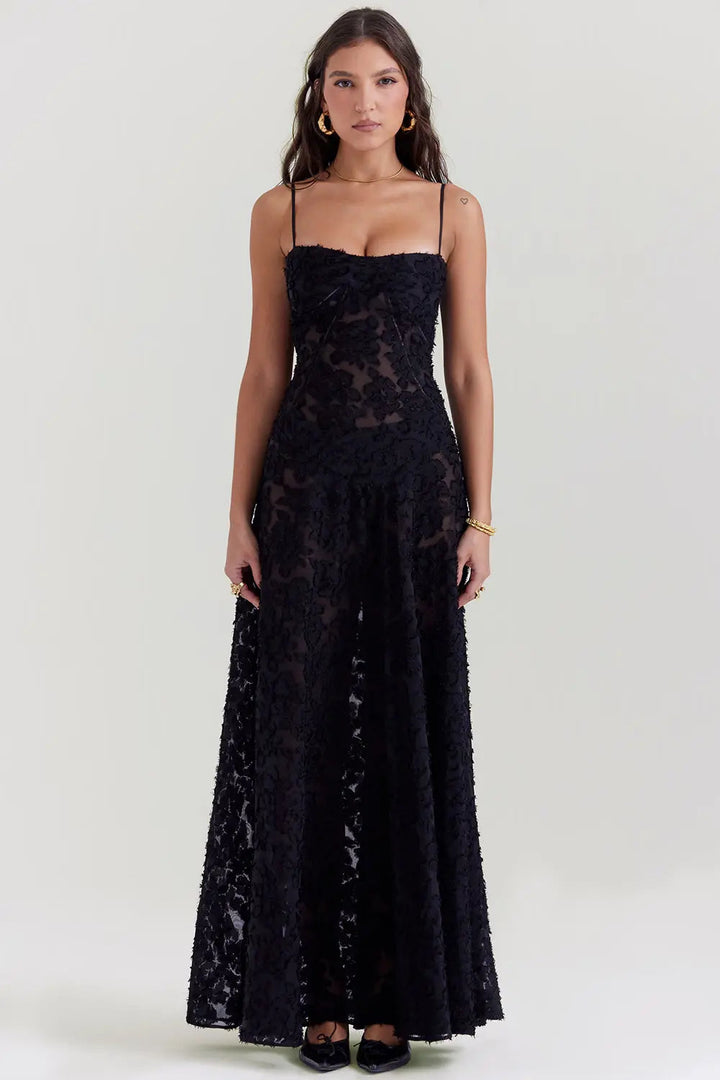 Woman wearing a flowing maxi dress with open back against a plain background.