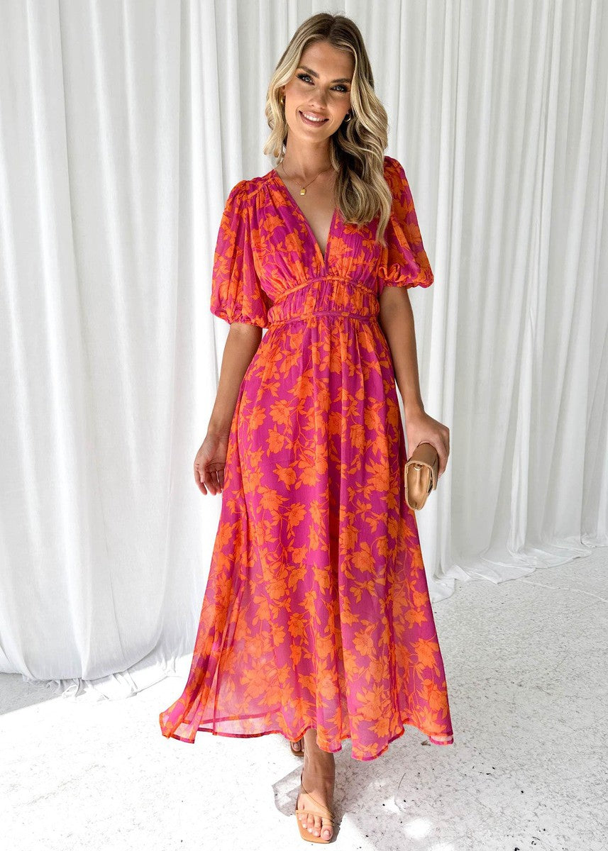 Female model wearing a floral V-neck maxi dress with a flowing silhouette against a plain background.
