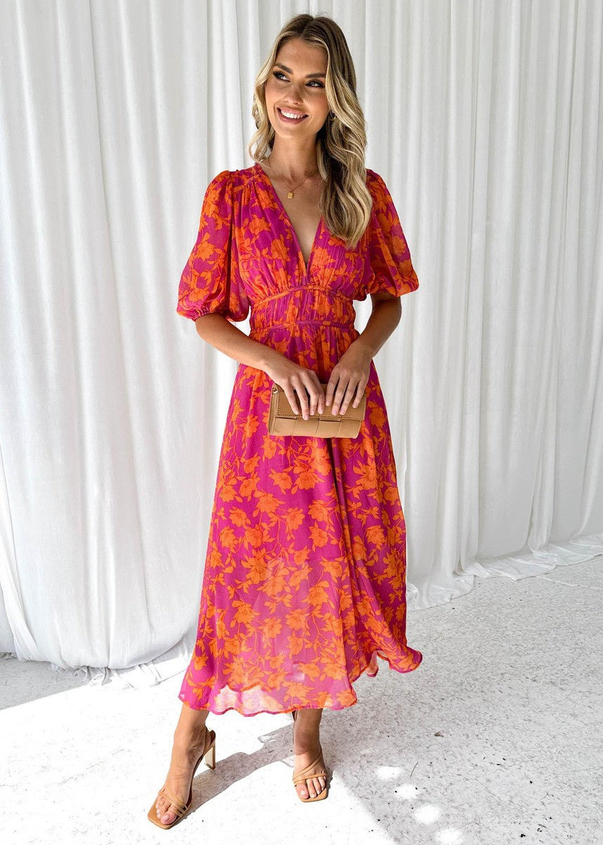 Woman in a vibrant floral maxi dress featuring a V-neckline and relaxed fit on a plain background.
