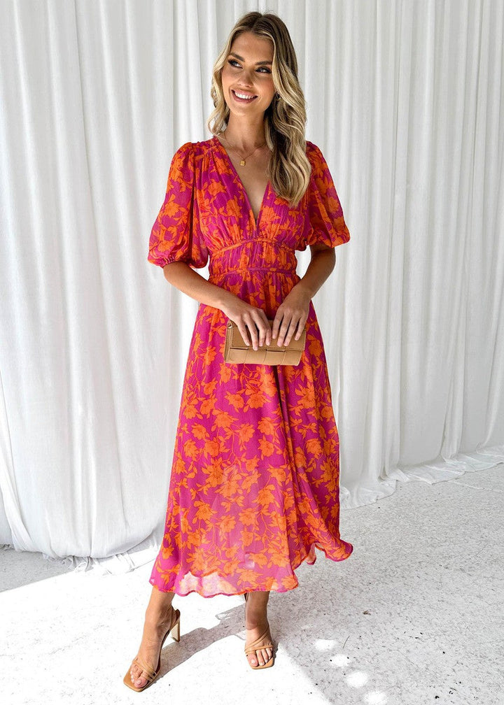 Woman in a vibrant floral maxi dress featuring a V-neckline and relaxed fit on a plain background.
