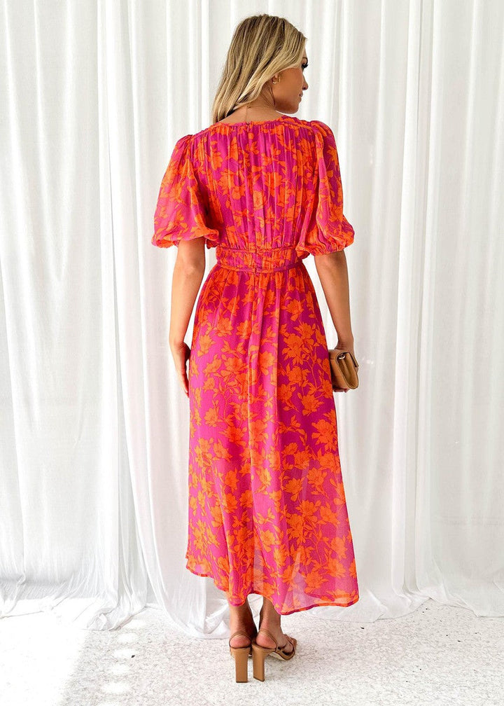 Woman wearing a colourful V-neck maxi dress designed for summer occasions against a plain background.