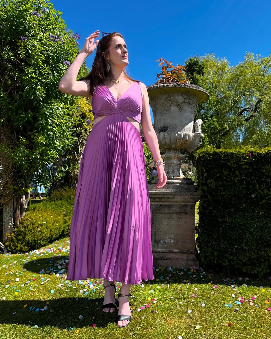 Female model displaying a flowing midi dress with pleated texture against a plain backdrop.