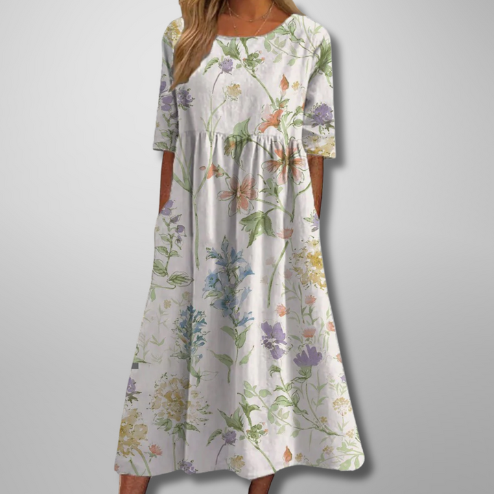 Model in a floral empire waist maxi dress with side pockets on a plain background.