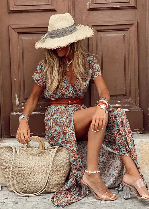 Woman model wearing a flowing floral dress with a rustic wooden background.