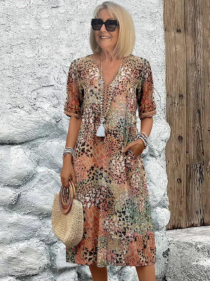 Woman model posing in a vibrant printed midi dress with functional pockets on a clean background.