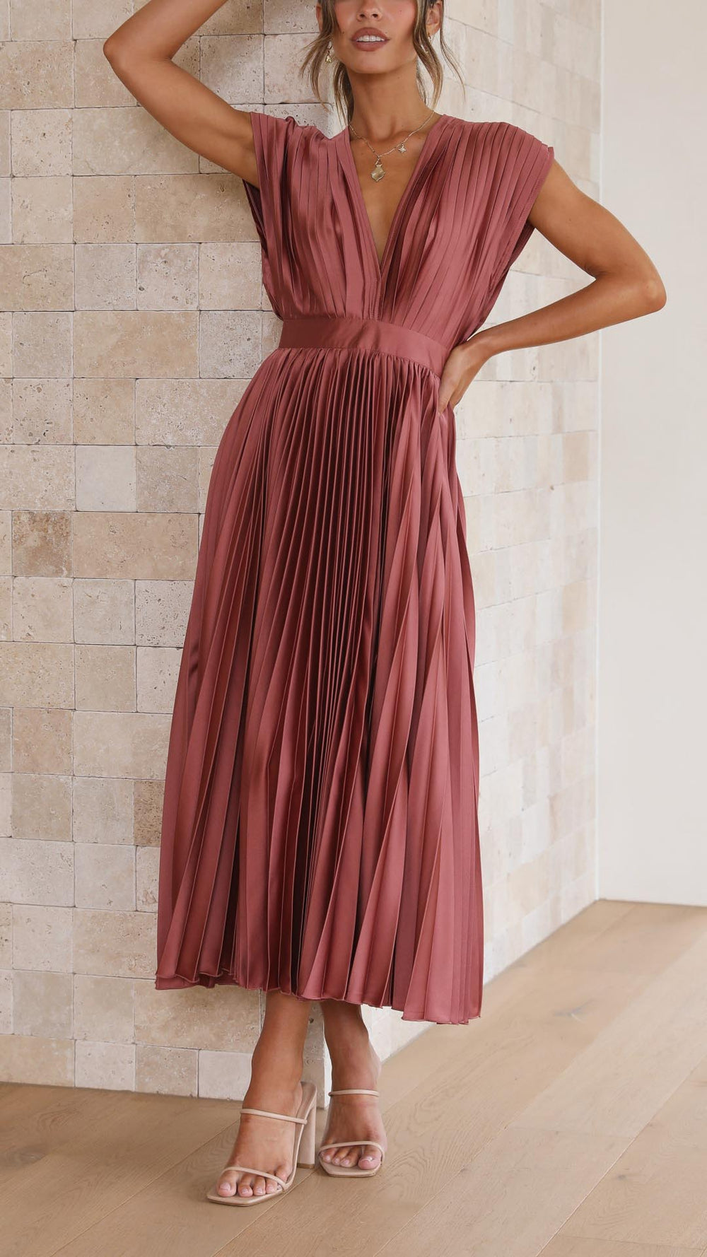 Woman model in a V-neck pleated midi dress against a plain background.