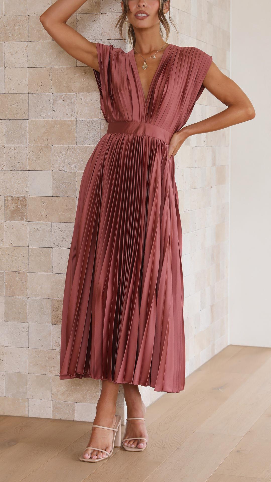Woman model in a V-neck pleated midi dress against a plain background.