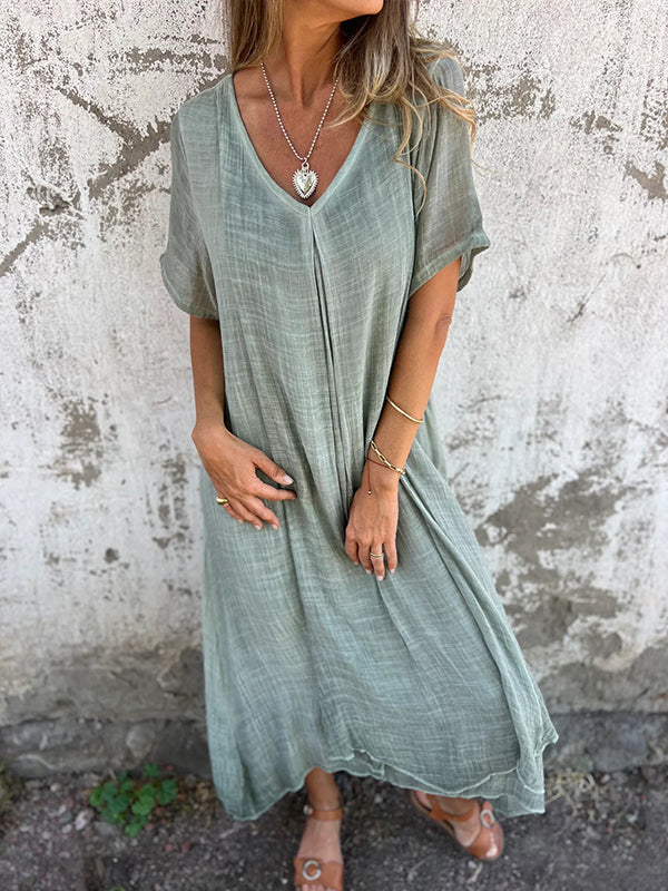 Model in a relaxed casual dress with V-neck design on a cement background.