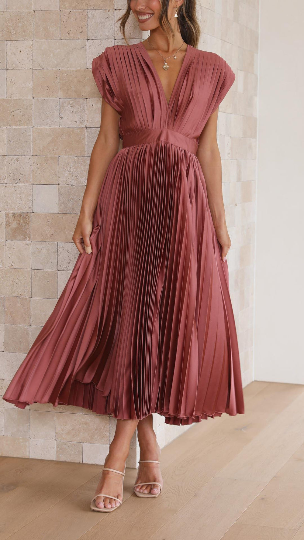 Woman showcasing a flowing pleated midi dress with a V-neck design on a plain background.
